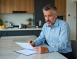 Homme d'âge moyen lisant des documents immobiliers dans une cuisine moderne